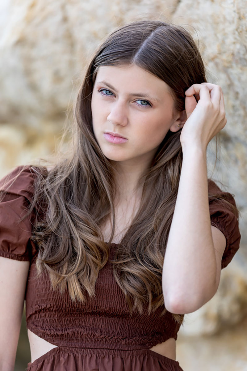 Le Portrait & Mode 29 Portrait d'une jeune fille blonde aux yeux bleus en robe marron élégante, debout sur une plage en lumière naturelle
