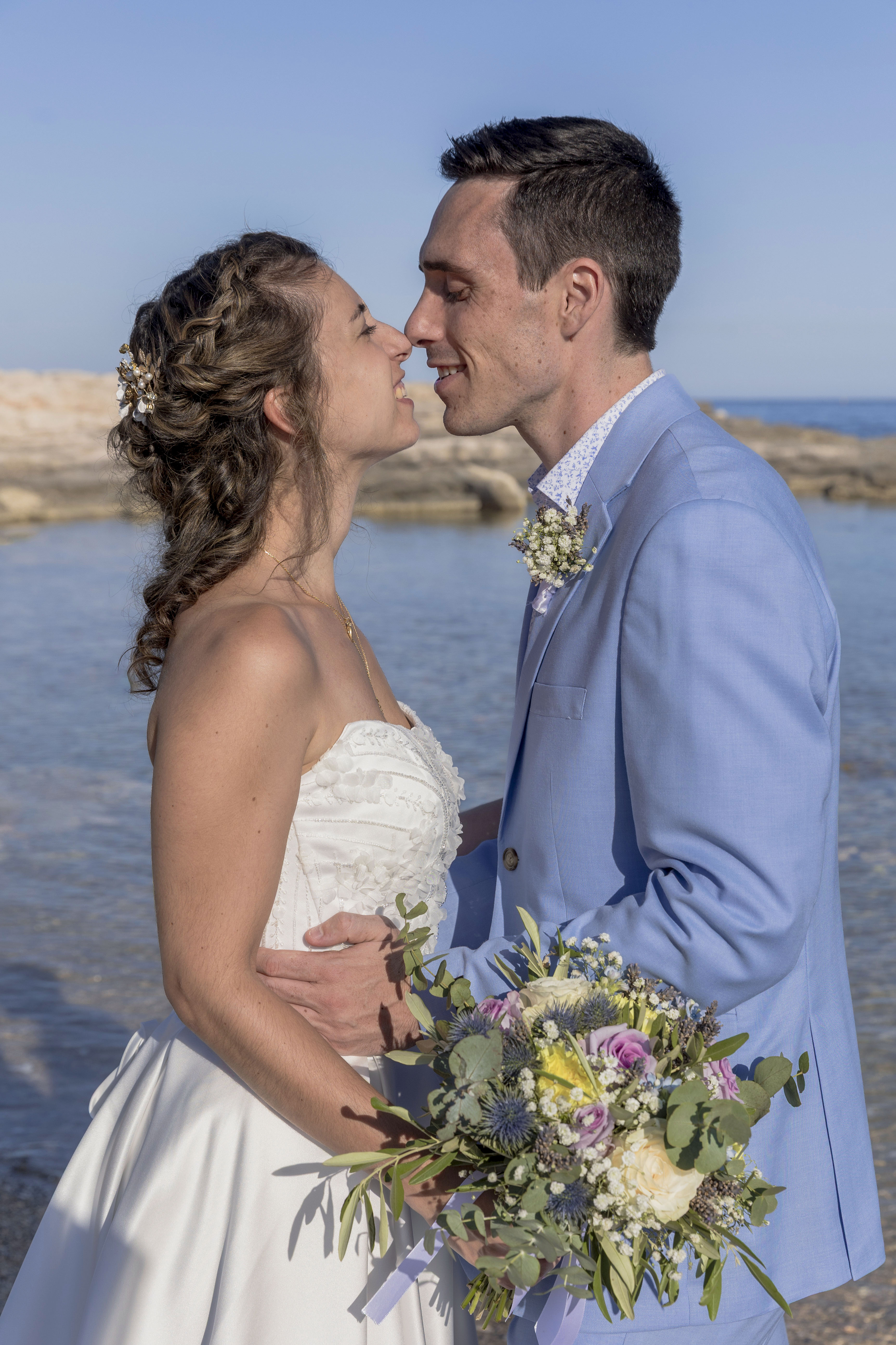 Mariés s’embrassant sur la plage avec bouquet coloré face à la mer – photographie naturelle par M.Studiophoto13