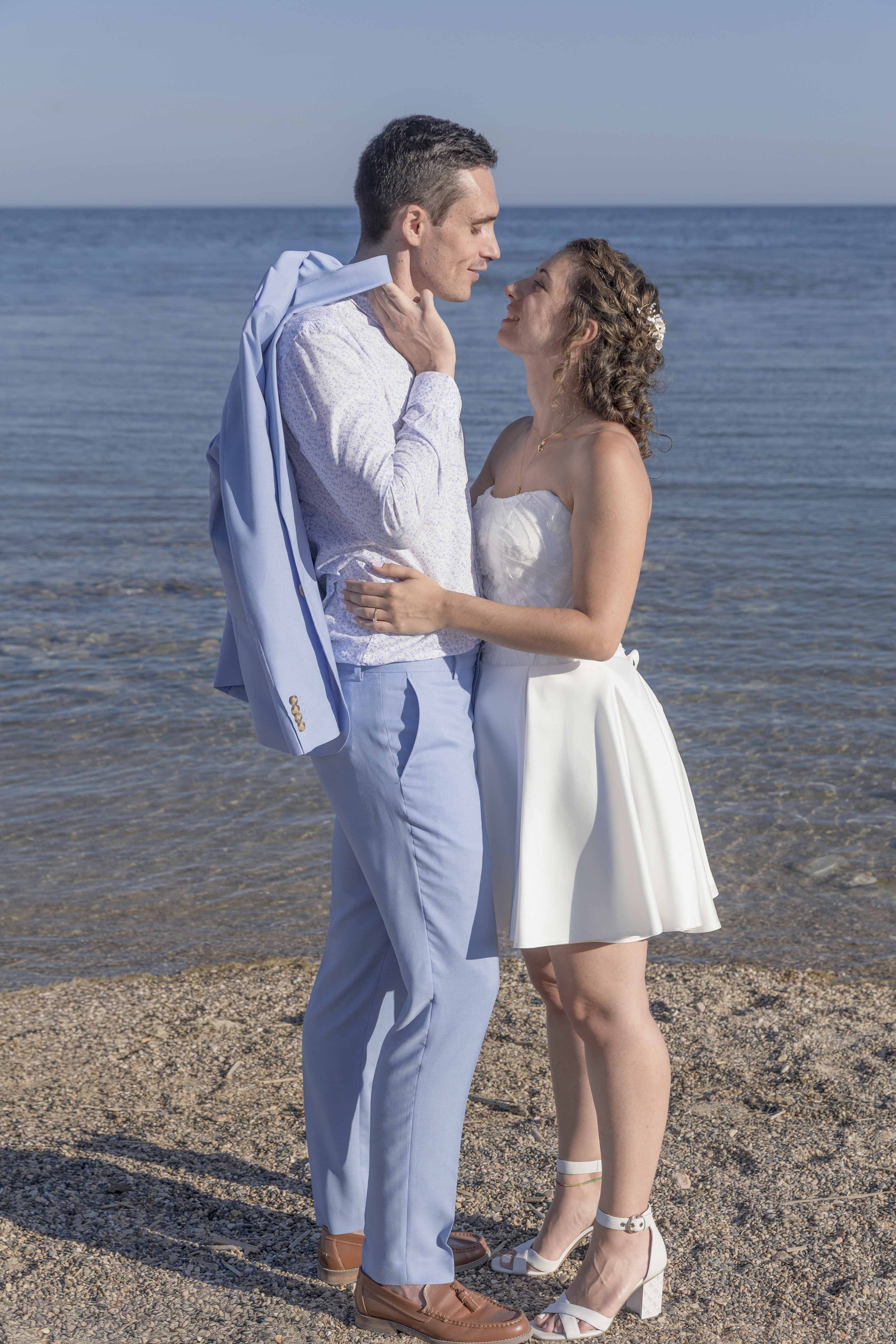 Couple de mariés enlacés sur la plage face à la mer, photographie de mariage romantique sur la Côte Bleue par M.Studiophoto13