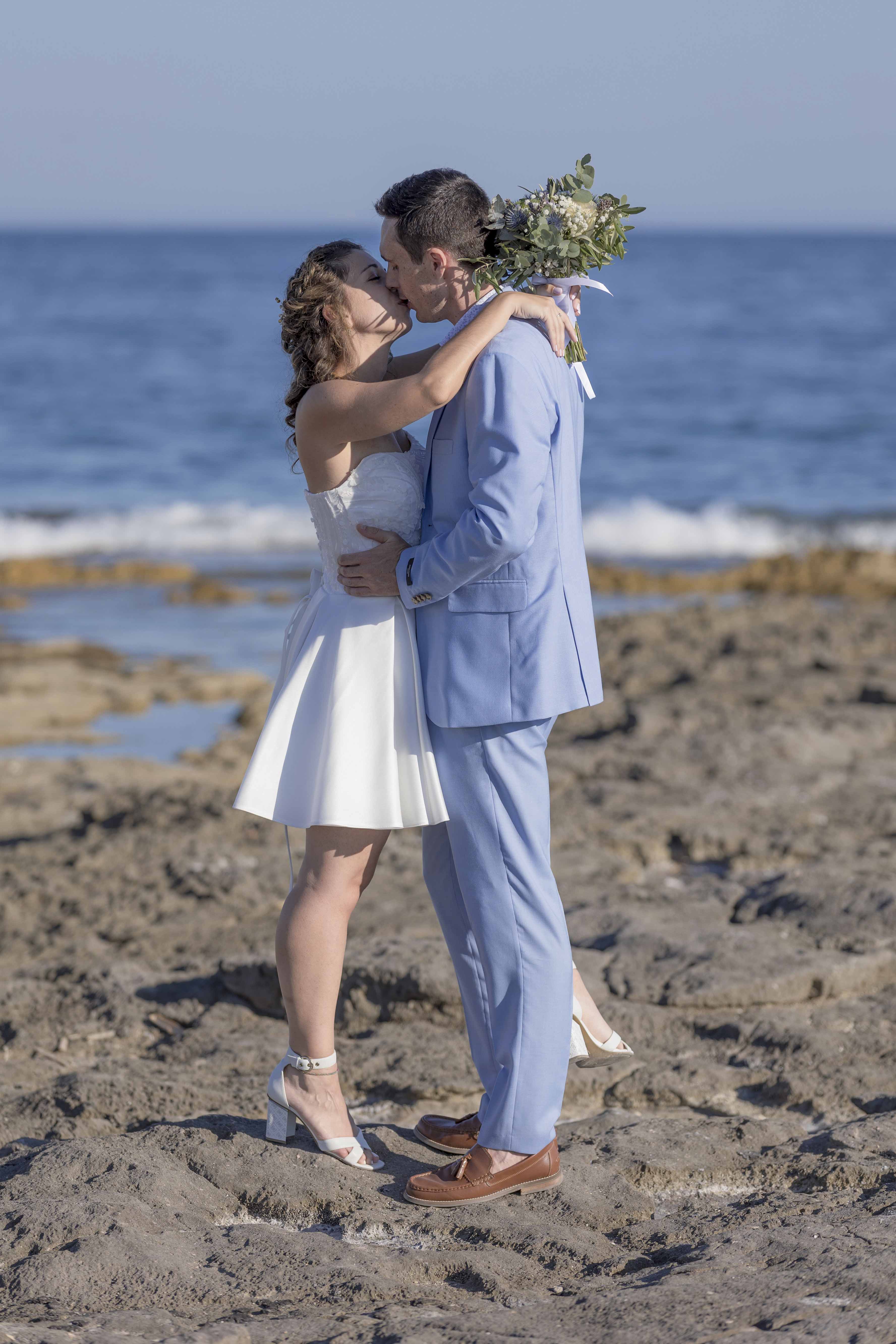 Mariés s’embrassant sur les rochers en bord de mer, bouquet à la main – photographie romantique de mariage par M.Studiophoto13