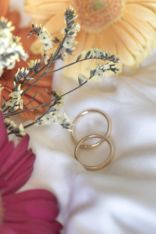 Alliances de mariage dorées posées sur un bouquet de fleurs coloré, photo de détail par M.Studiophoto13